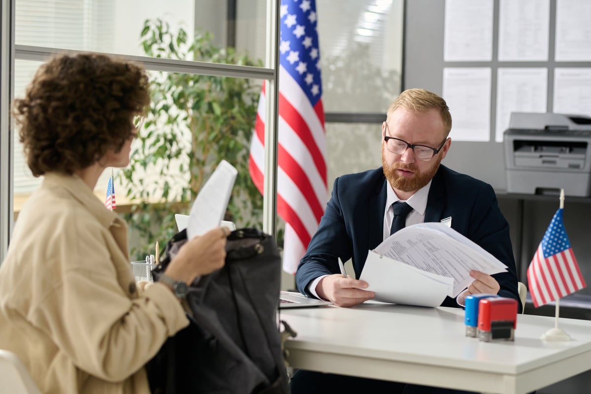 Oficial consular revisando documentos de solicitante durante entrevista de visa americana en oficina de inmigración de Estados Unidos
