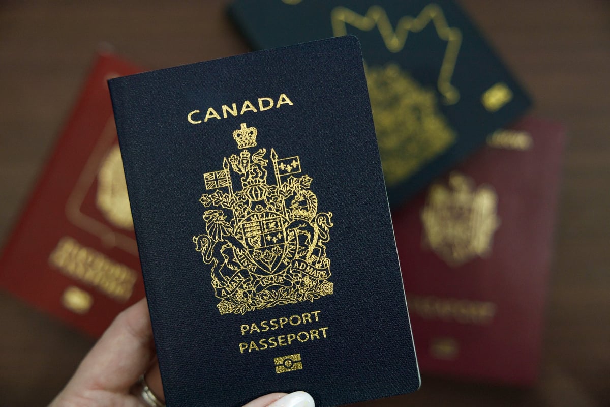 Vancouver, Canada - A hand holding a navy blue Canadian passport, with blurred international passports visible in the background
