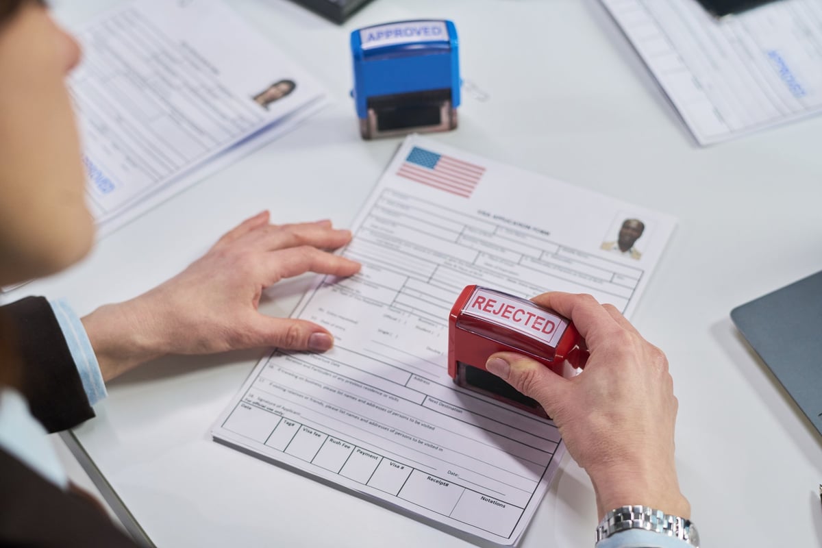 Oficial consular sellando formulario de visa americana con sello de rechazo durante proceso de evaluación